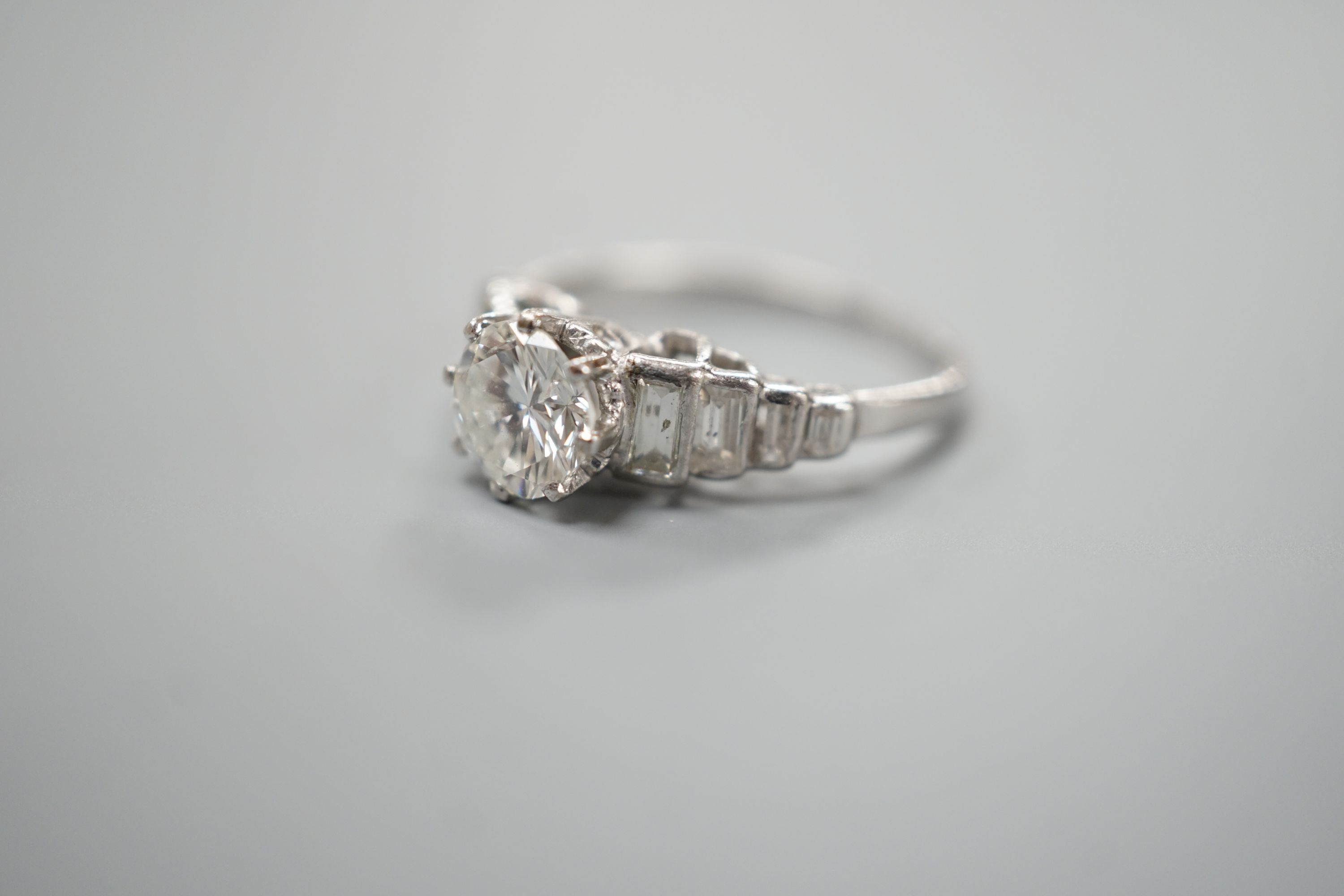 A white metal (stamped Plat) and single stone diamond ring, with graduated eight stone baguette cut diamond set shoulders, size K/L, gross weight 3.5 grams